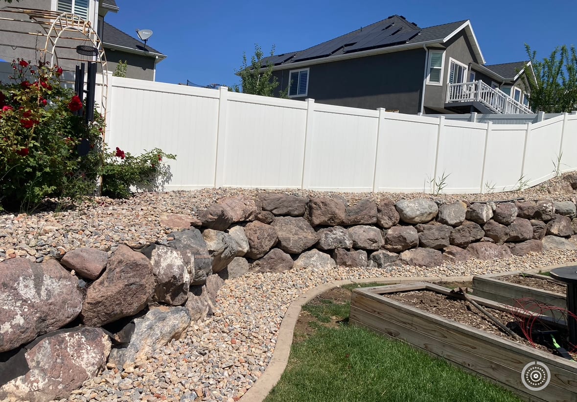 Rock retaining wall and hardscape landscaping along a Utah backyard fence